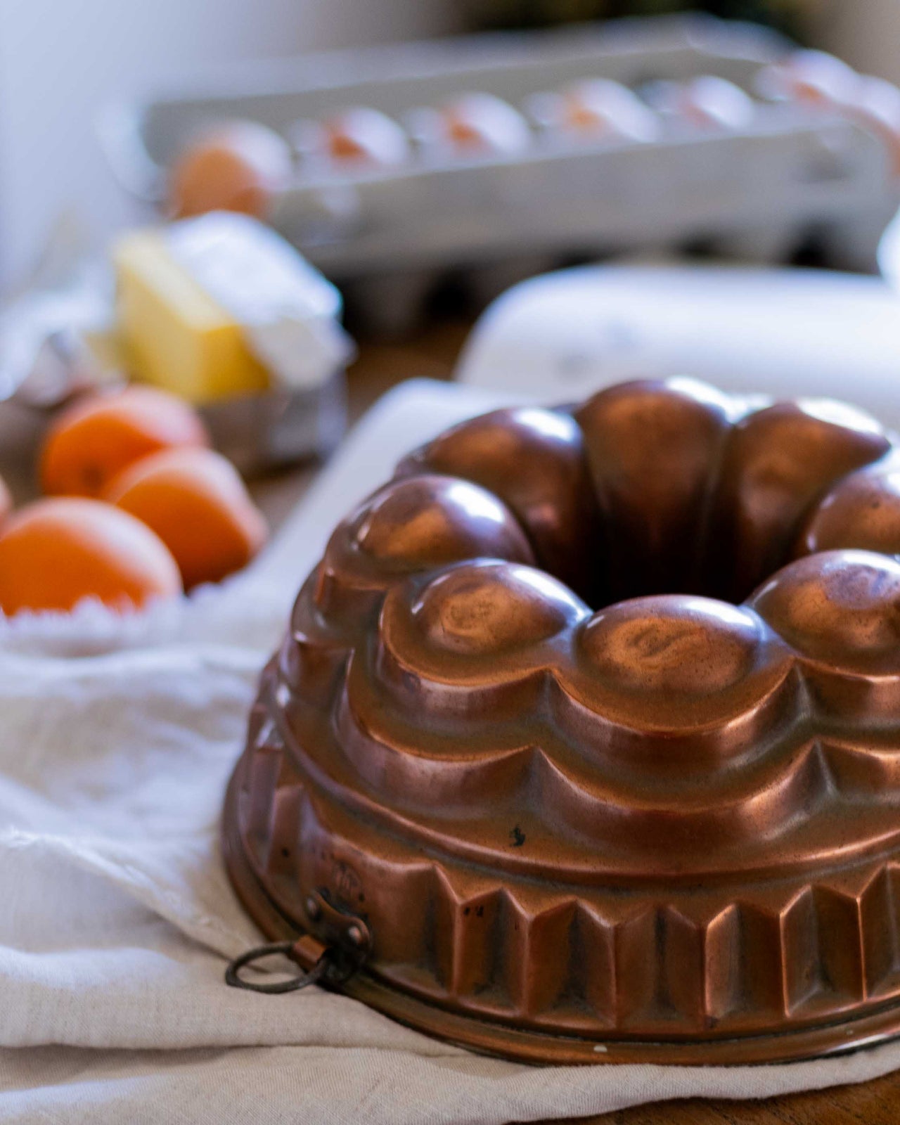 Copper Bundt cake mold on a kitchen counter with eggs and a carton in the background.