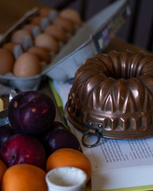 Copper Bundt cake pan on a surface with plums and an egg carton in the background