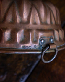Close-up of a textured copper mould with a hook on a wooden surface