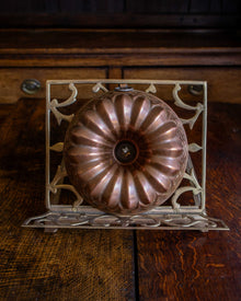 Copper bundt cake mould on a decorative metal stand against a wooden background