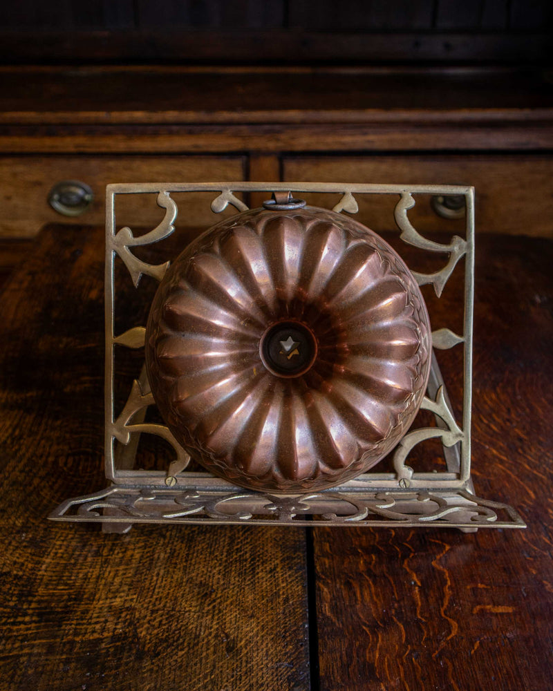 Copper bundt cake mould on a decorative metal stand against a wooden background