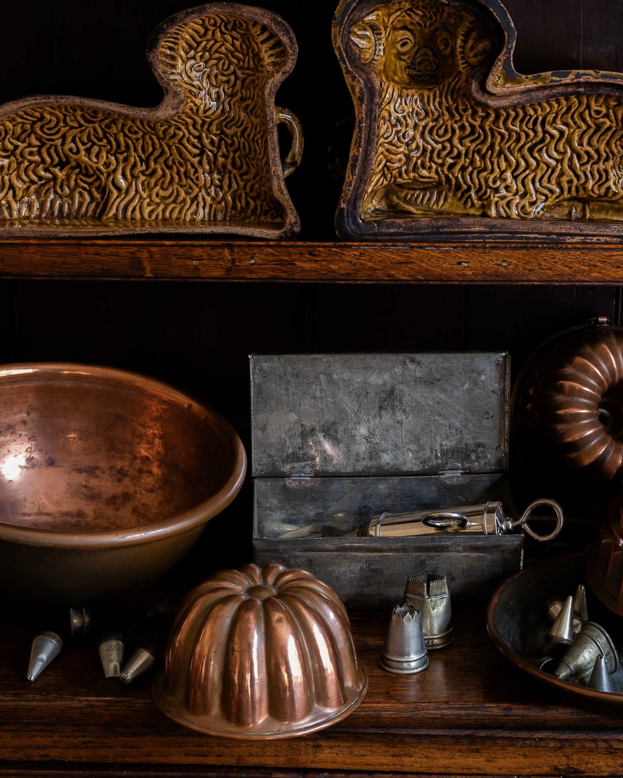 Collection of vintage kitchen utensils including a copper bowl, icing tips, and a copper mould on a wooden surface.