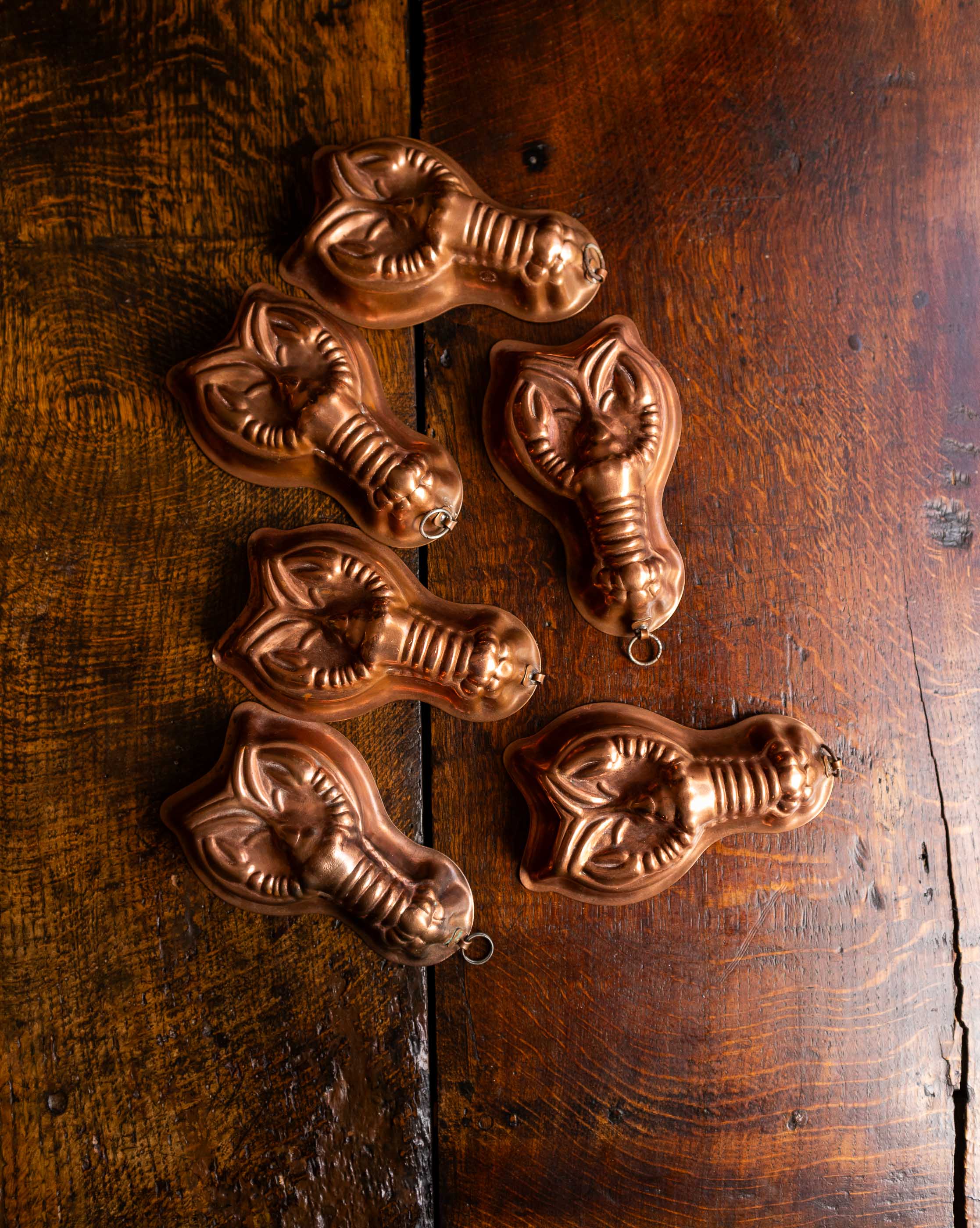 Set of six copper lobster moulds on a wooden surface
