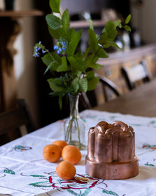 Copper mould on a table with apricots and a vase of flowers