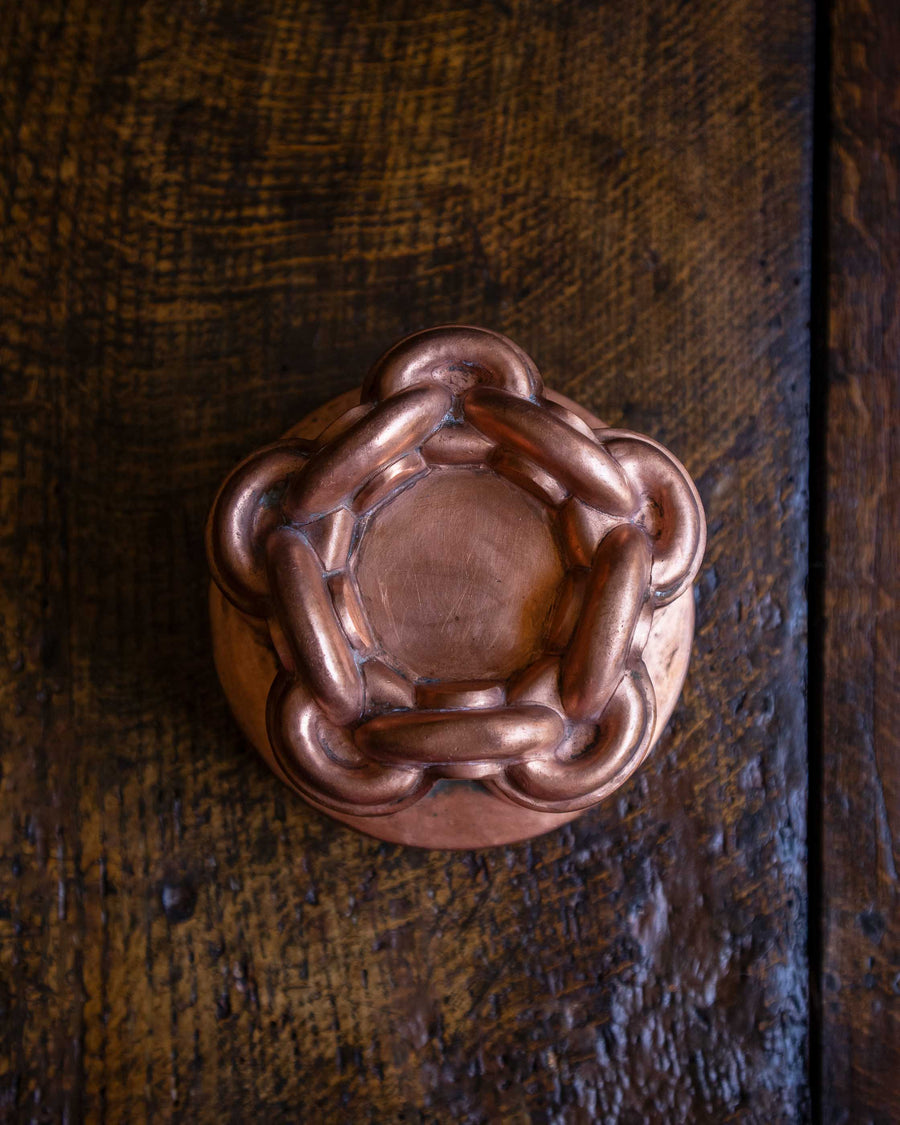 Close-up of a copper chain knot jelly mould on a wooden surface.