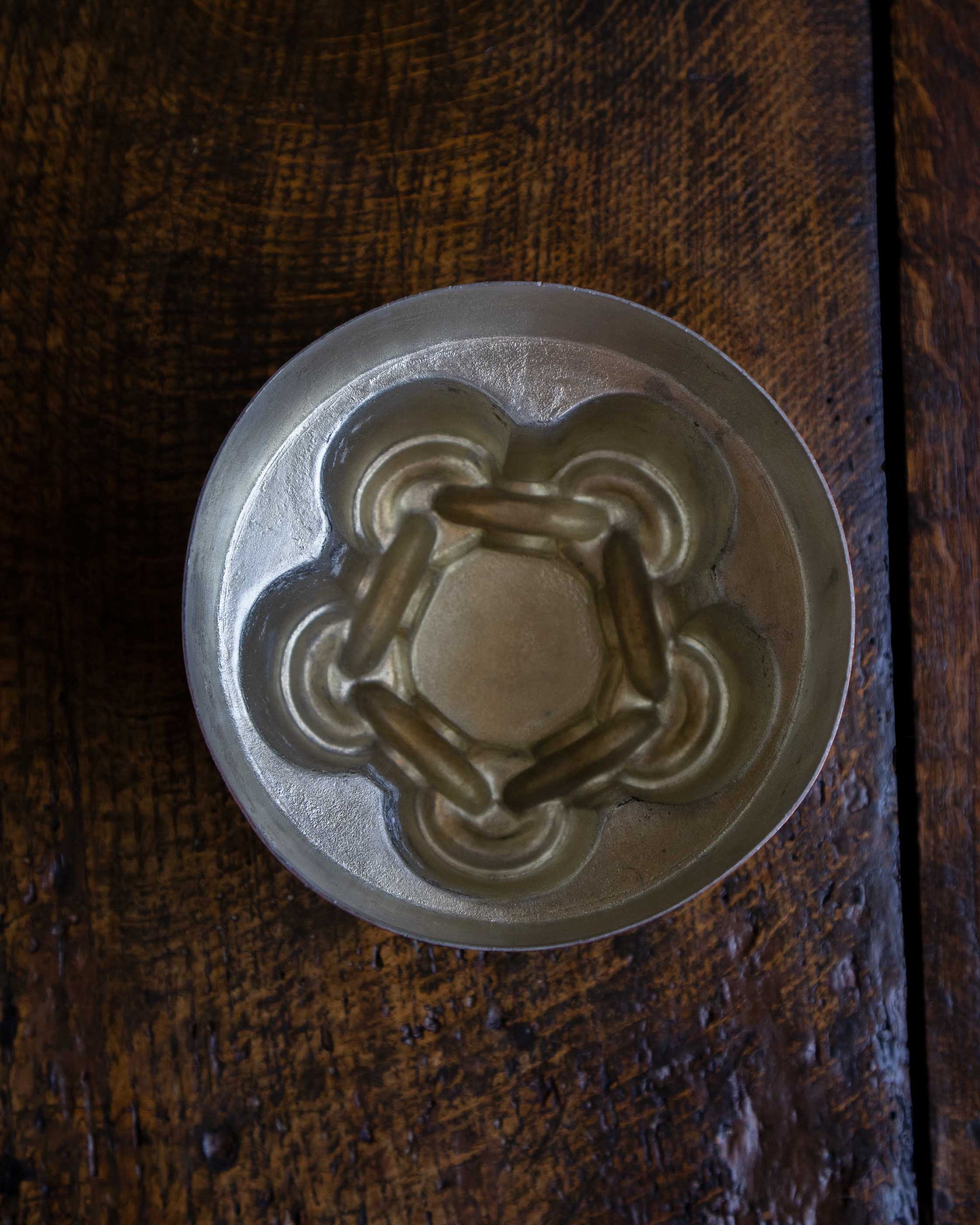 Close-up of a copper chain knot jelly mould on a wooden surface.