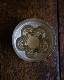 Close-up of a copper chain knot jelly mould on a wooden surface.