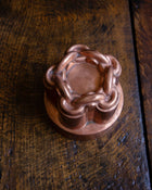 Close-up of a copper chain knot jelly mould on a wooden surface.