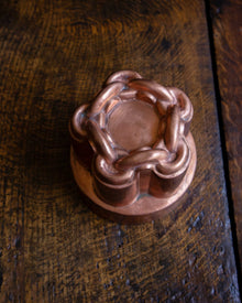 Close-up of a copper chain knot jelly mould on a wooden surface.
