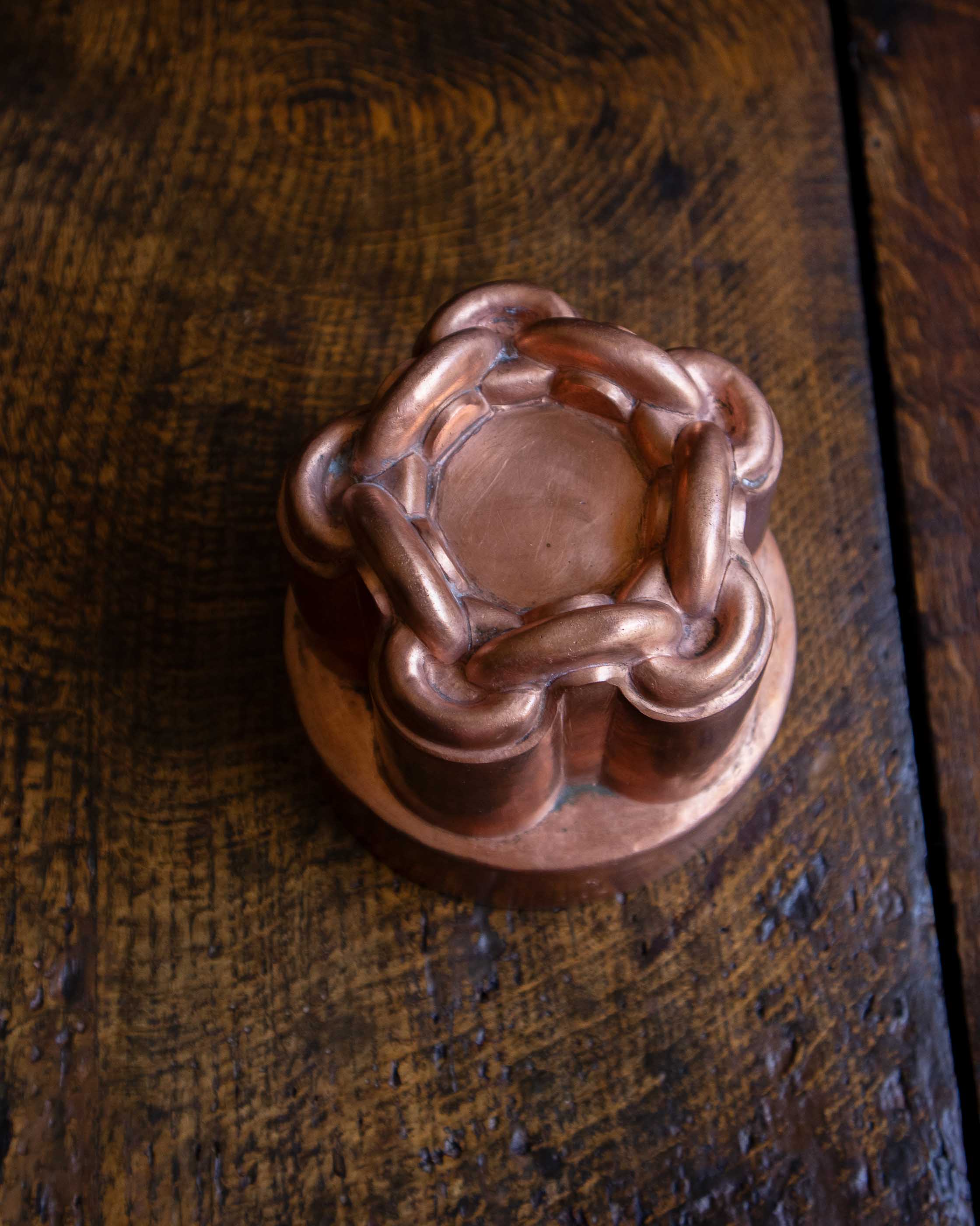 Close-up of a copper chain knot jelly mould on a wooden surface.