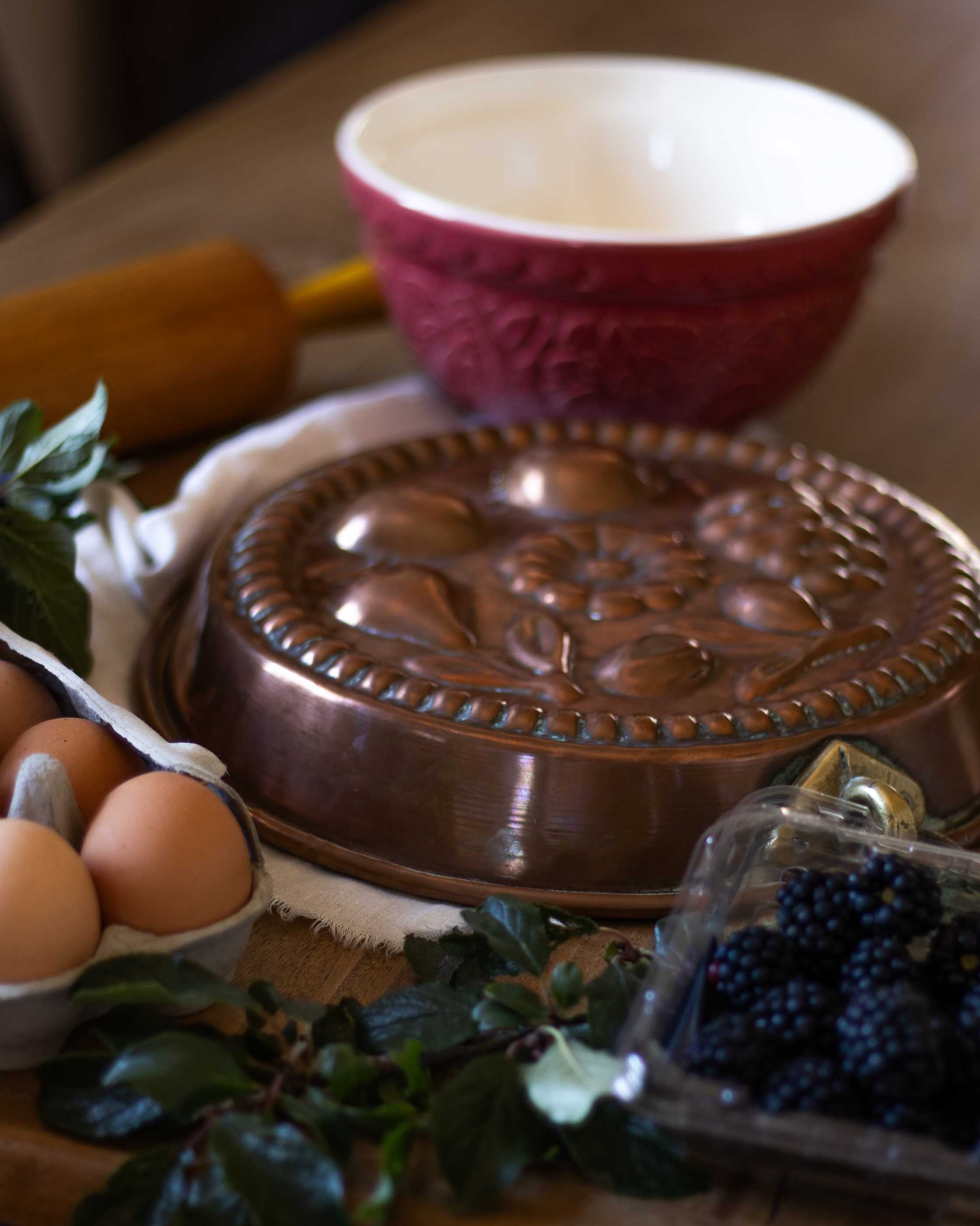 Copper mould, eggs, berries, and a red bowl on a wooden surface