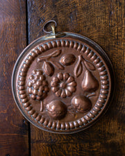 Decorative copper mould with fruit design on a wooden surface