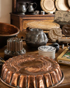 Collection of vintage kitchenware including copper moulds, metal pots, and wooden breadboards on a wooden surface.