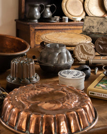 Collection of vintage kitchenware including copper moulds, metal pots, and wooden breadboards on a wooden surface.