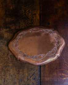 Decorative copper tray with engraved design on a wooden surface