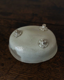 White ceramic mould with three small peg feet on a dark wooden surface