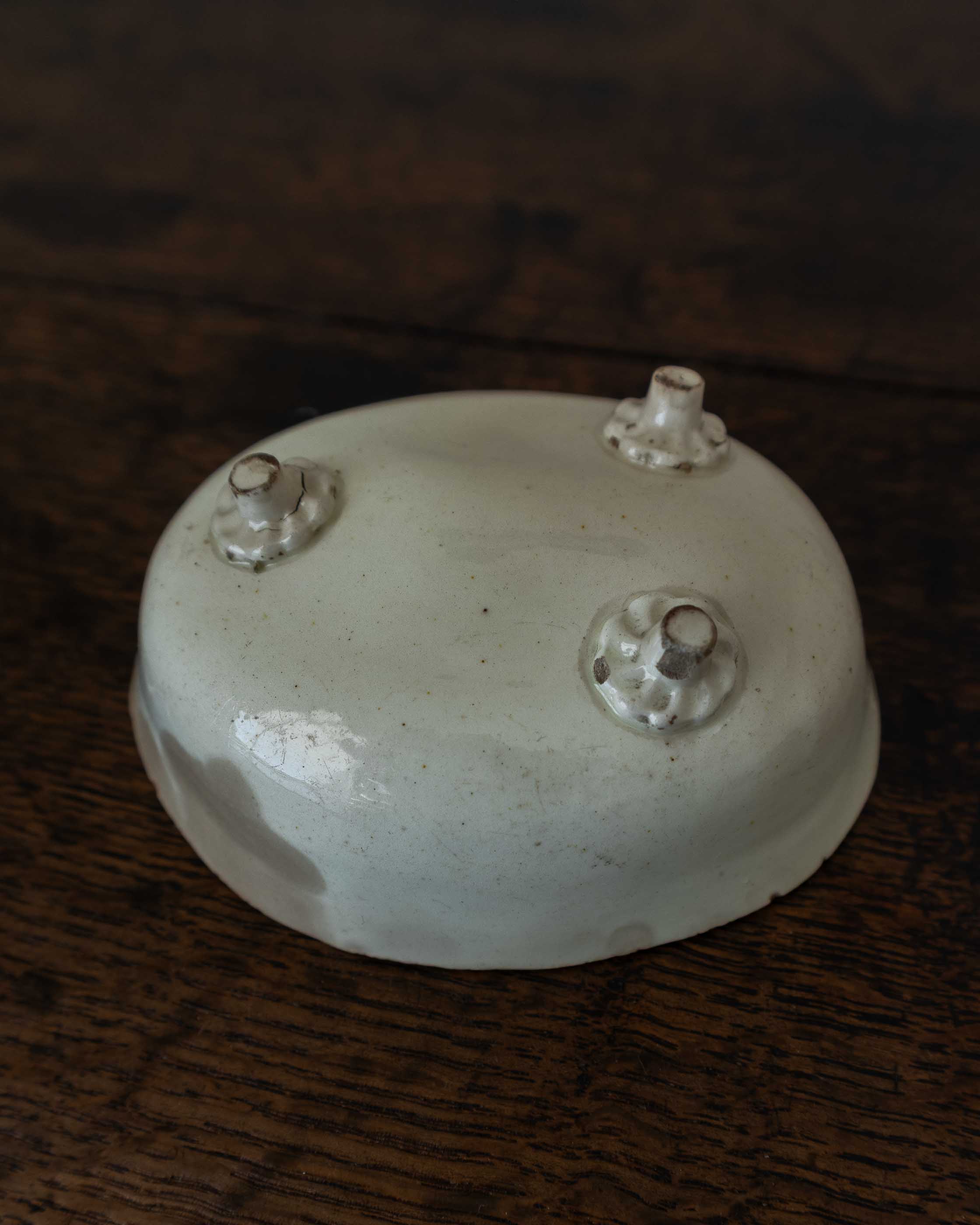 White ceramic mould with three small peg feet on a dark wooden surface