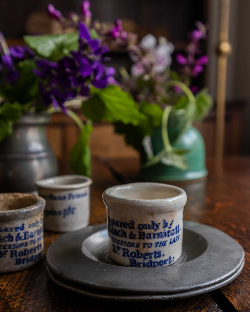 Ceramic pots with text on a wooden table with flowers in the background