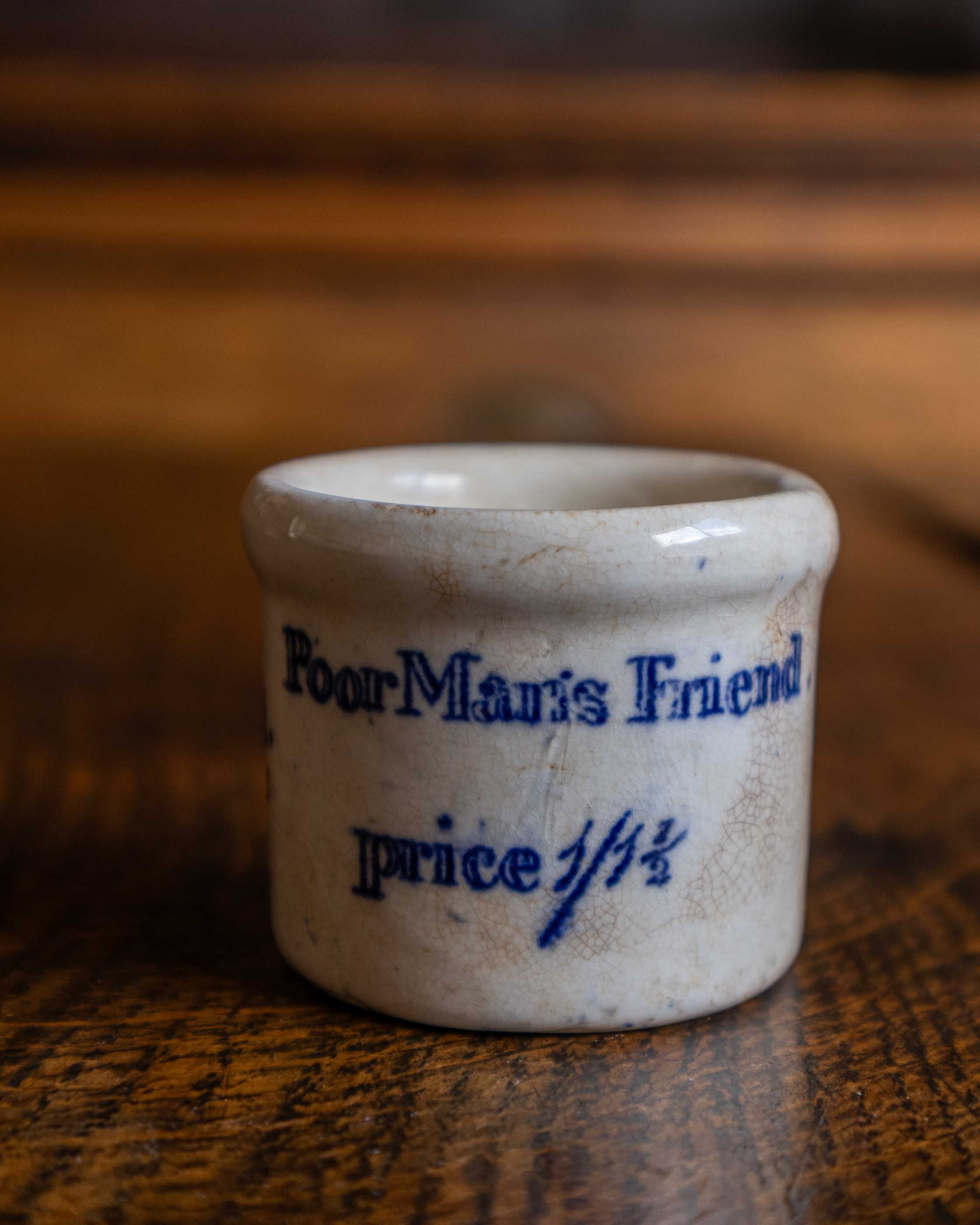 Small ceramic pot with 'Poor Man's Friend' text on a wooden surface