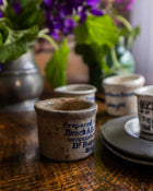 Ceramic pots with text and illustrations on a wooden surface with flowers in the background