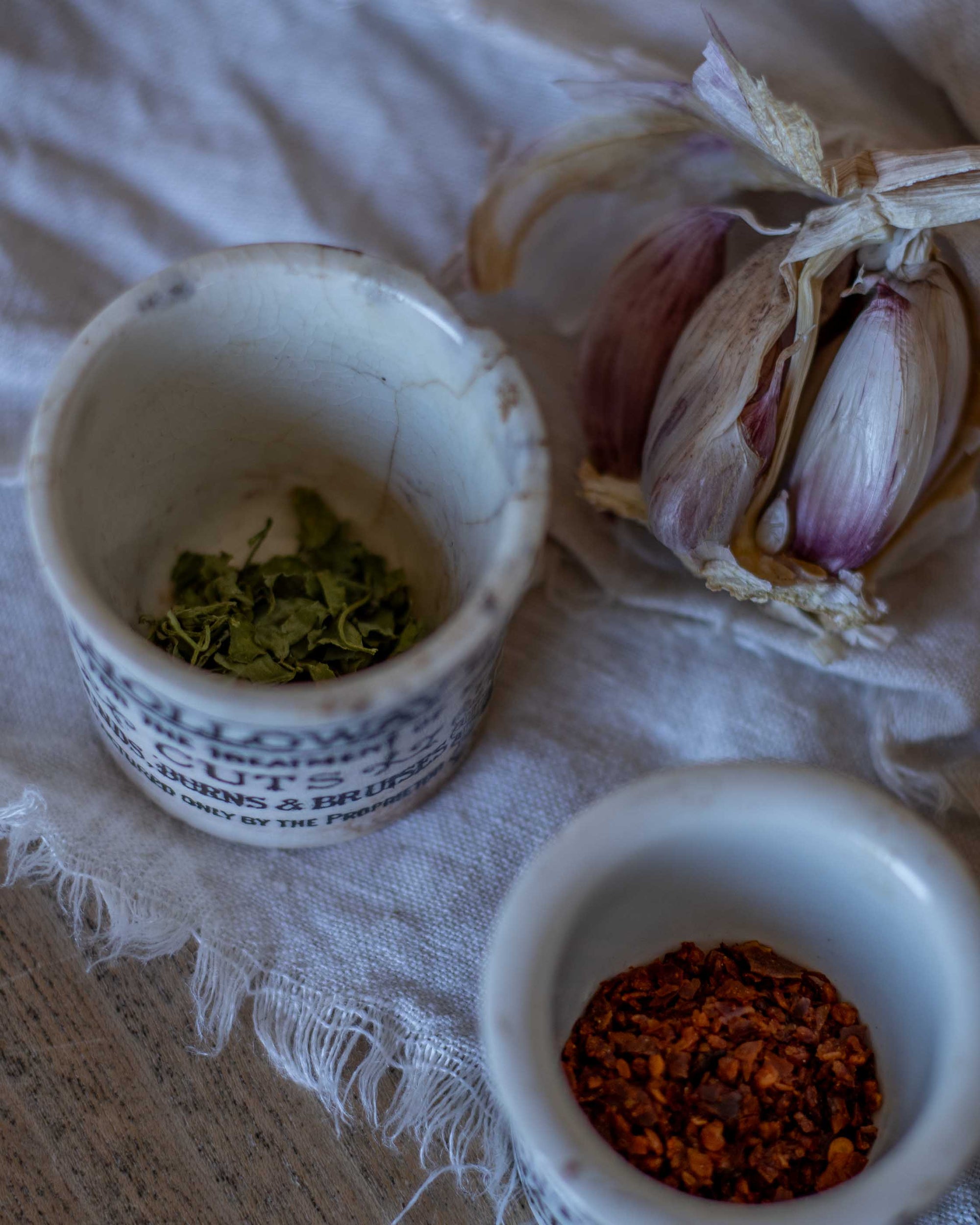 Two small ceramic pots with herbs and spices on a textured surface