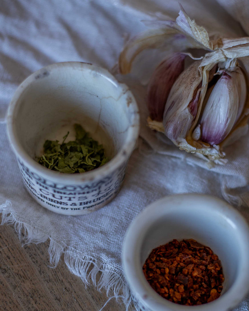 Two small ceramic pots with herbs and spices on a textured surface