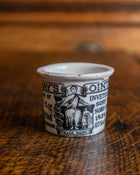 Small ceramic pot with black text and graphics on a wooden surface