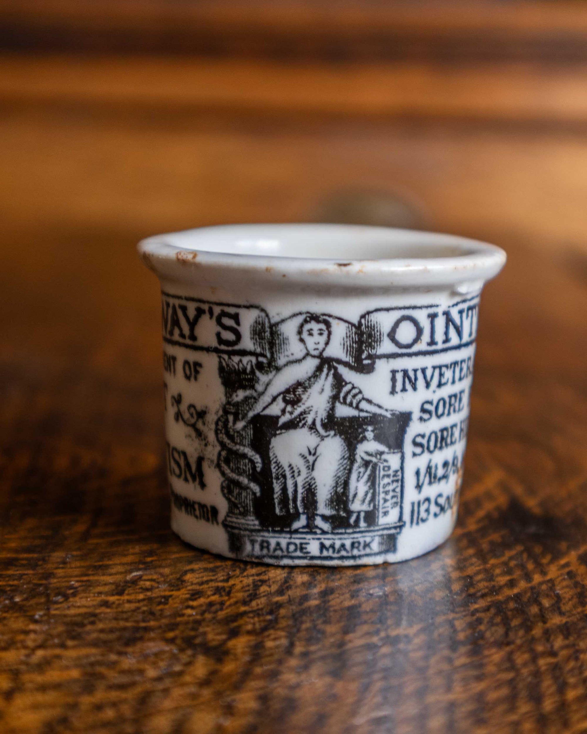 Small ceramic pot with black text and graphics on a wooden surface