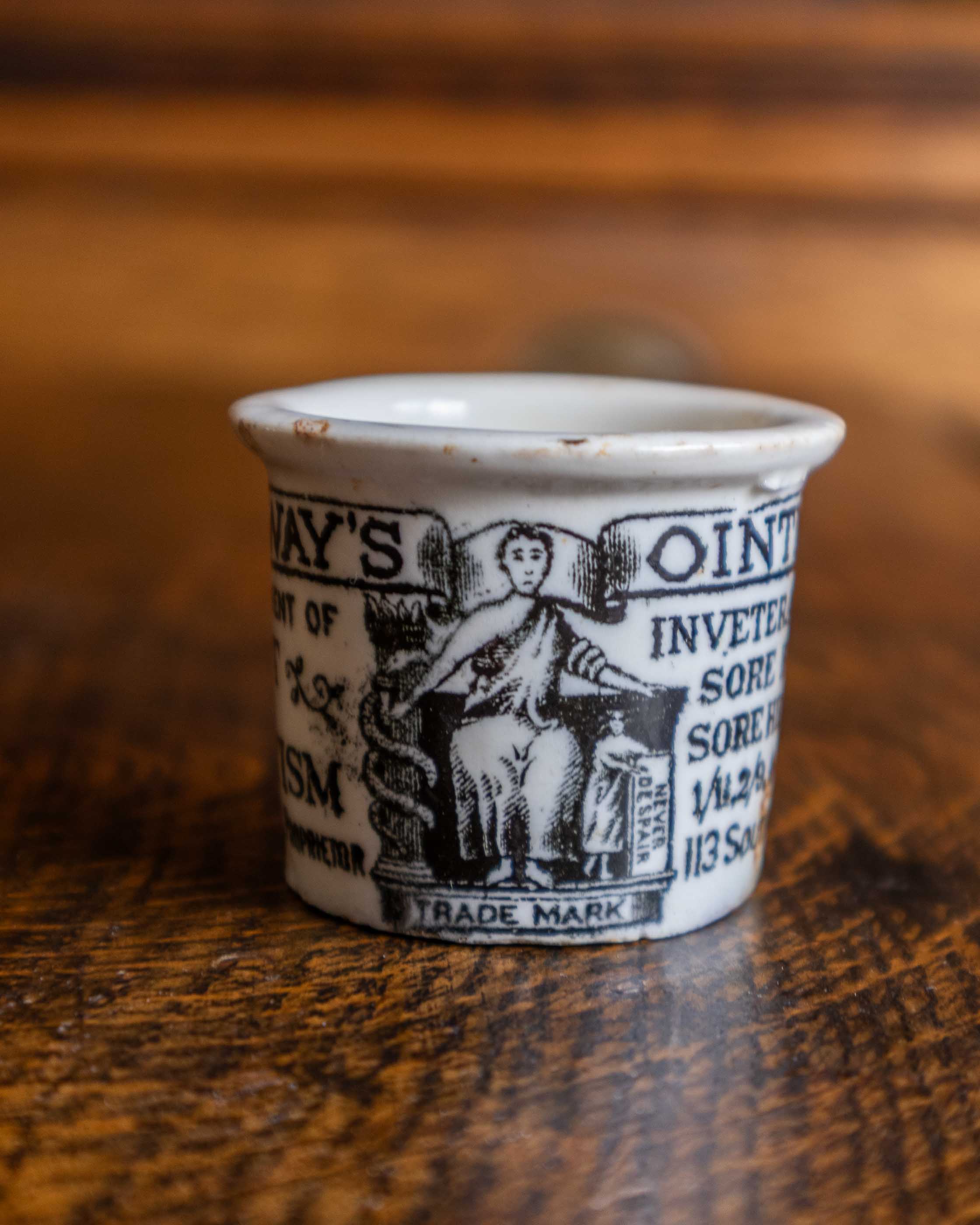 Small ceramic pot with black text and graphics on a wooden surface