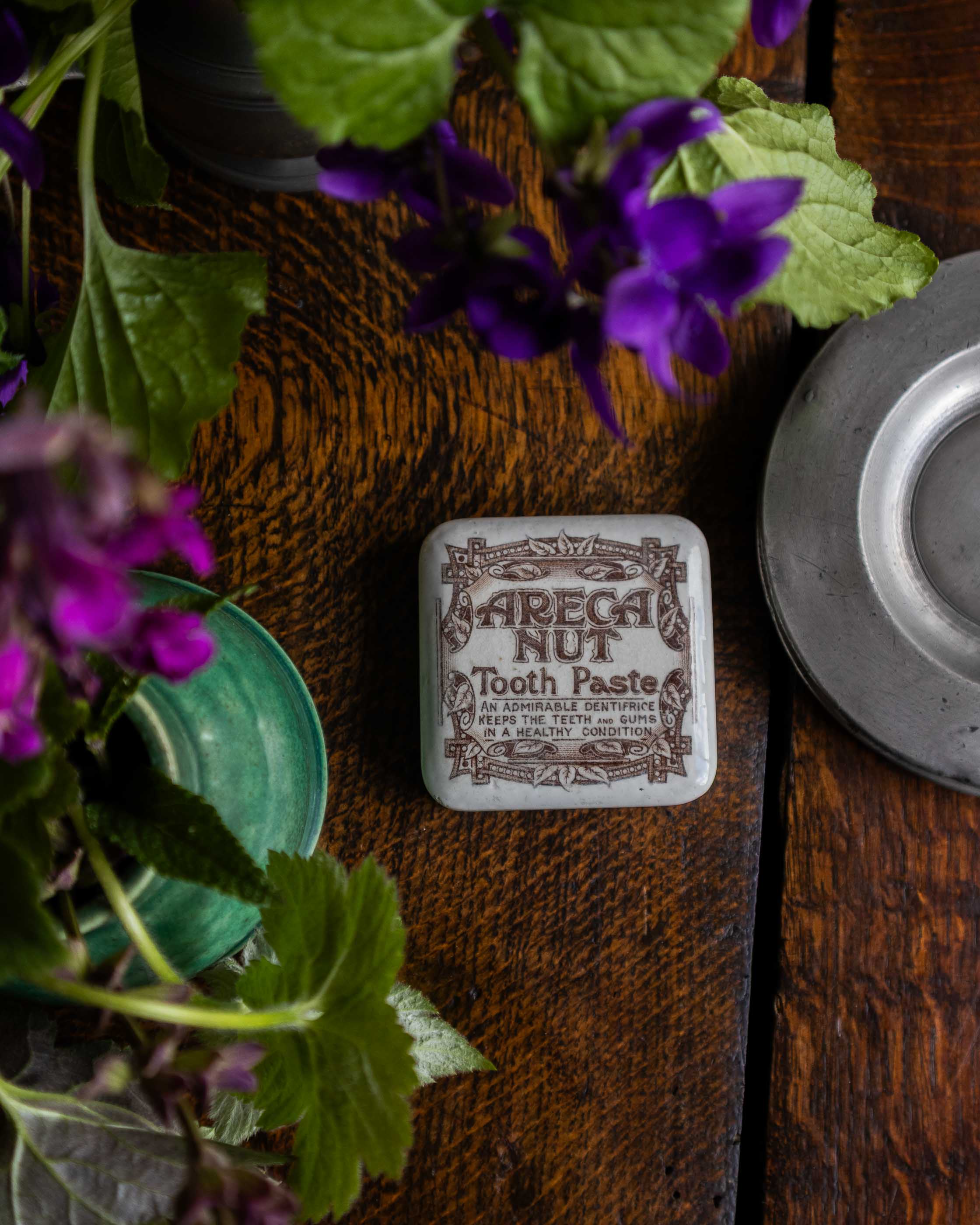 Areca Nut Tooth Paste lid on a wooden surface with purple flowers