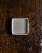 Small square white ceramic dish on a dark wooden surface