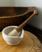 Mortar and pestle on a wooden surface with a wooden bowl in the background.
