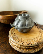 Pewter mould on a wooden surface with a wooden bowl in the background