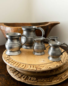 Set of pewter measures on a wooden breadboards with a wooden bowl in the background