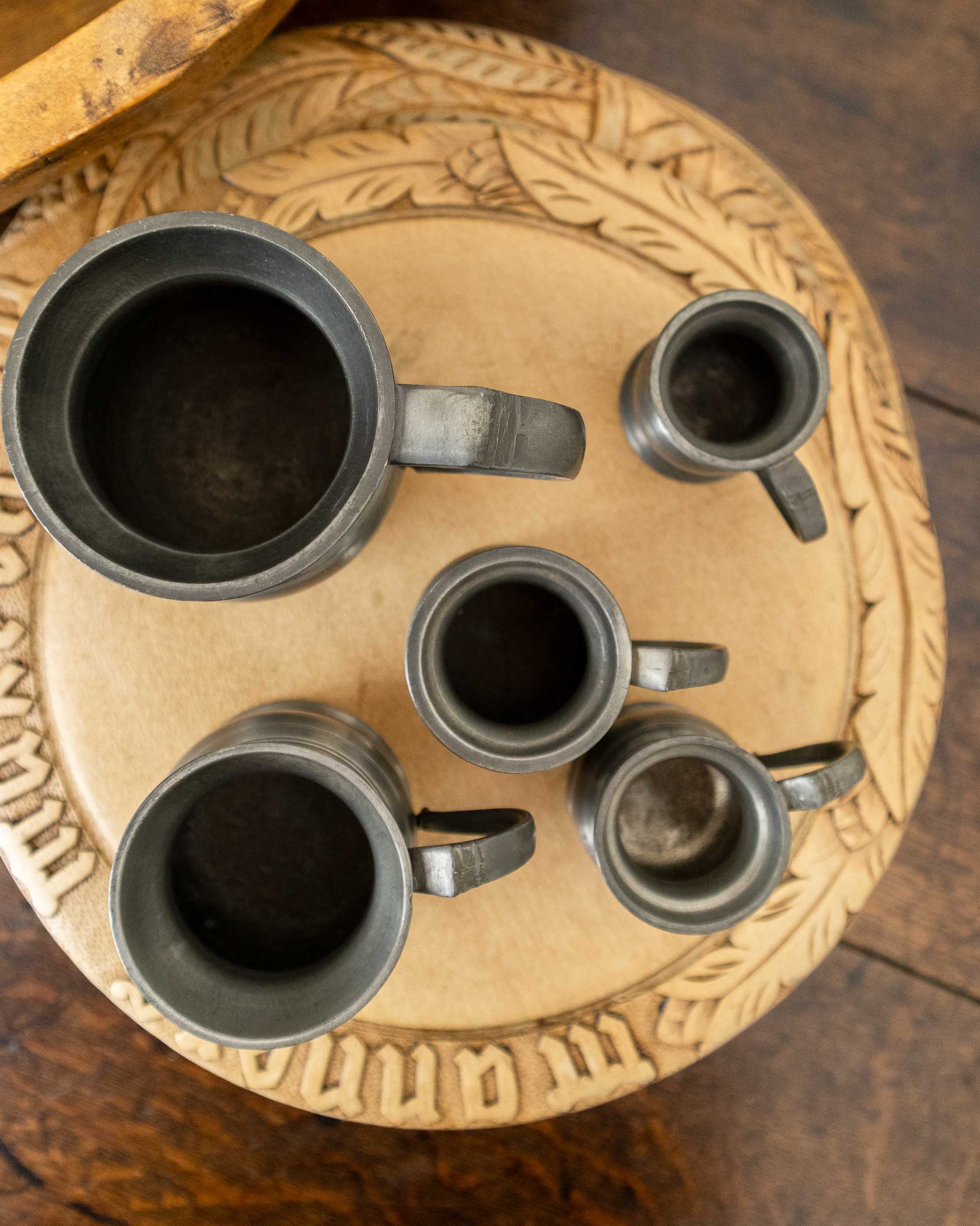 Five pewter measures on a decorative wooden tray