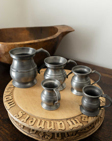 Set of five pewter measures on wooden breadboards with a wooden bowl in the background