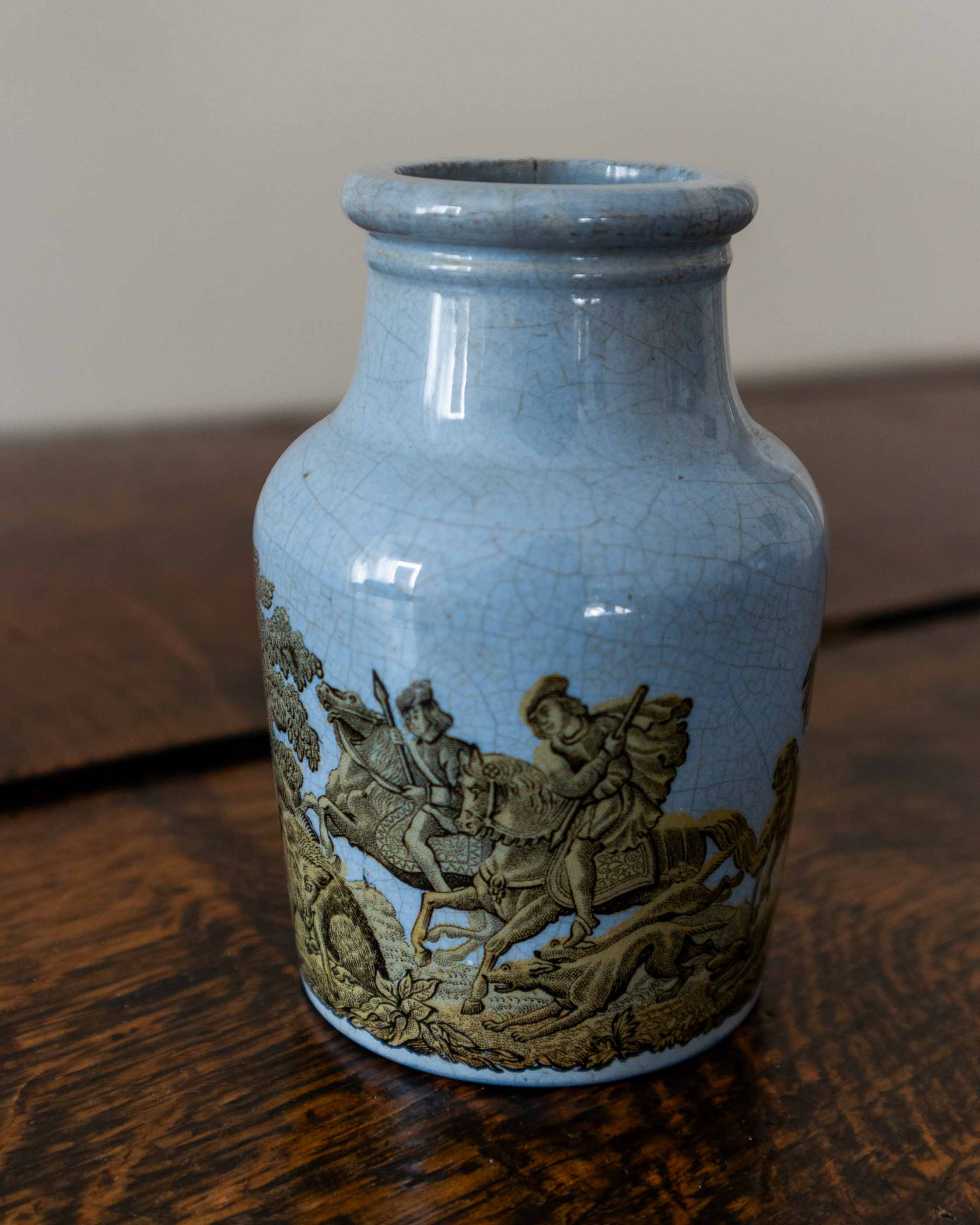 Blue ceramic jar with decorative horse and rider design on a wooden surface