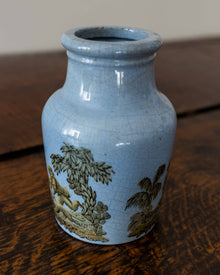 Blue ceramic jar with gold embossed design on a wooden surface