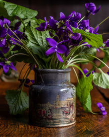 Purple flowers in a decorative prattware jar on a wooden surface