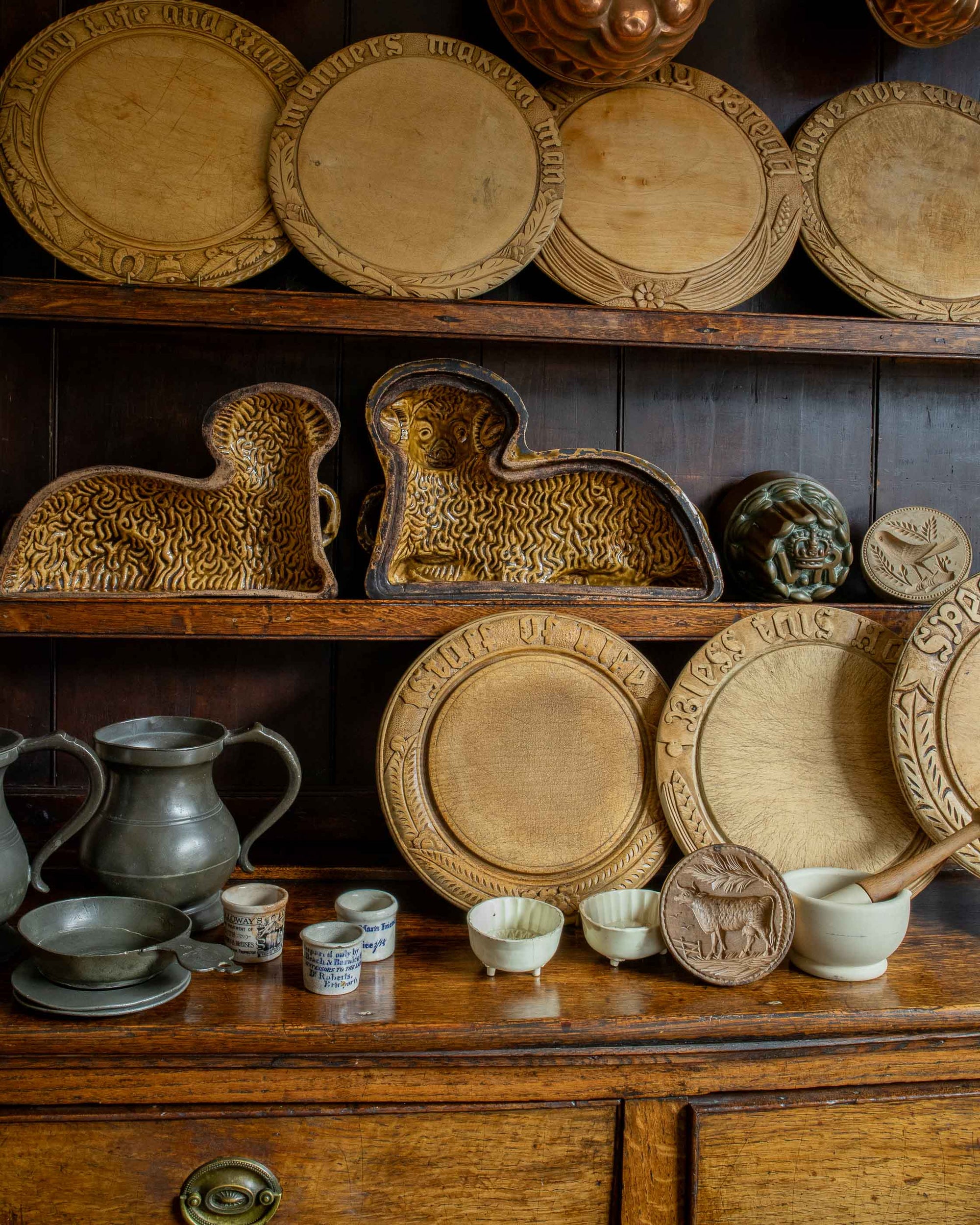 Collection of wooden breadboards and ceramic objects, bowls, and platters on a wooden shelf.