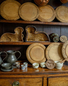 Collection of wooden breadboards and ceramic objects, bowls, and platters on a wooden shelf.
