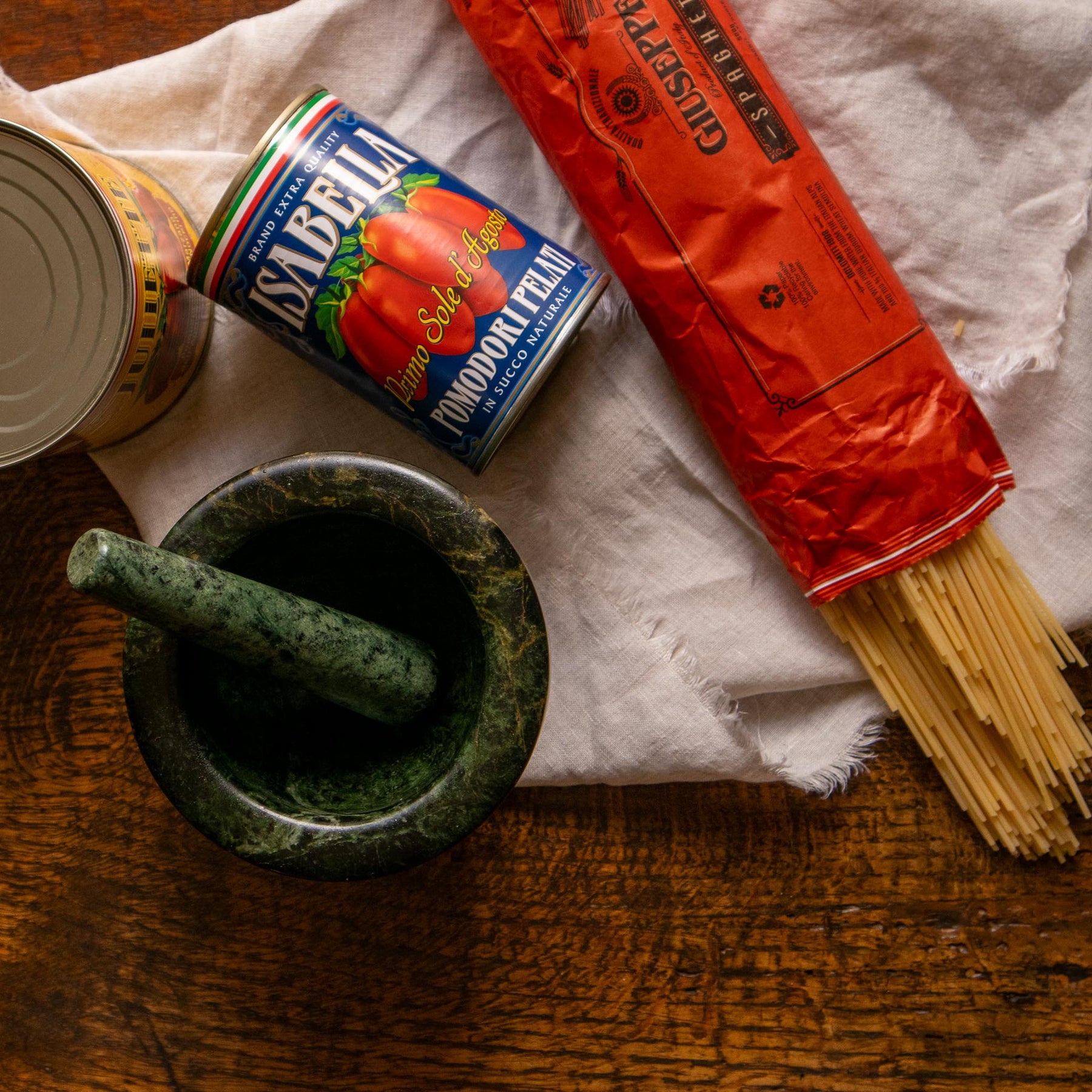 Mortar and pestle with a can of tomatoes and a package of pasta on a wooden surface