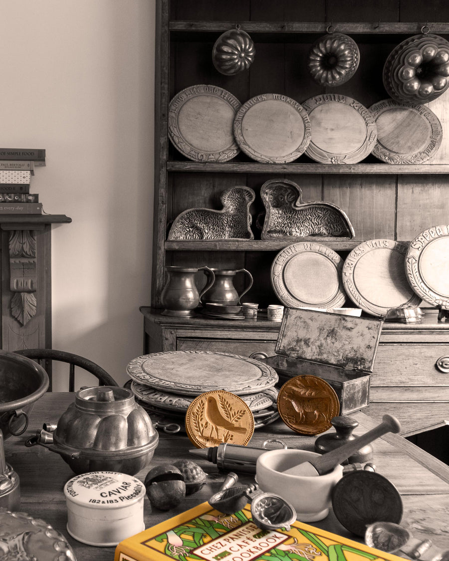 Vintage kitchen scene with wooden dresser displaying plates and jars, and a table with kitchen items.