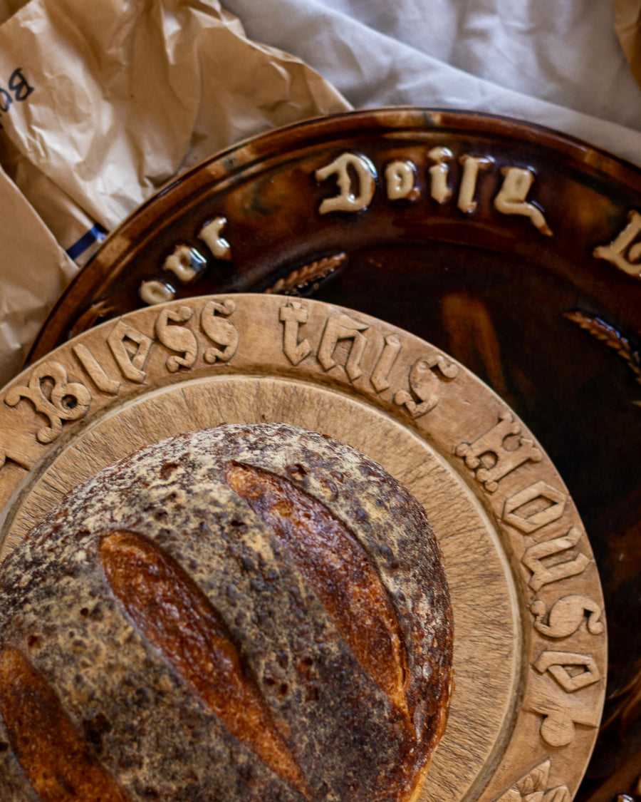 Loaf of bread on a wooden antique bread board with engraved text, placed on a white surface.