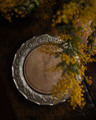 Decorative silver breadboard with engraved design on a wooden surface with yellow flowers.