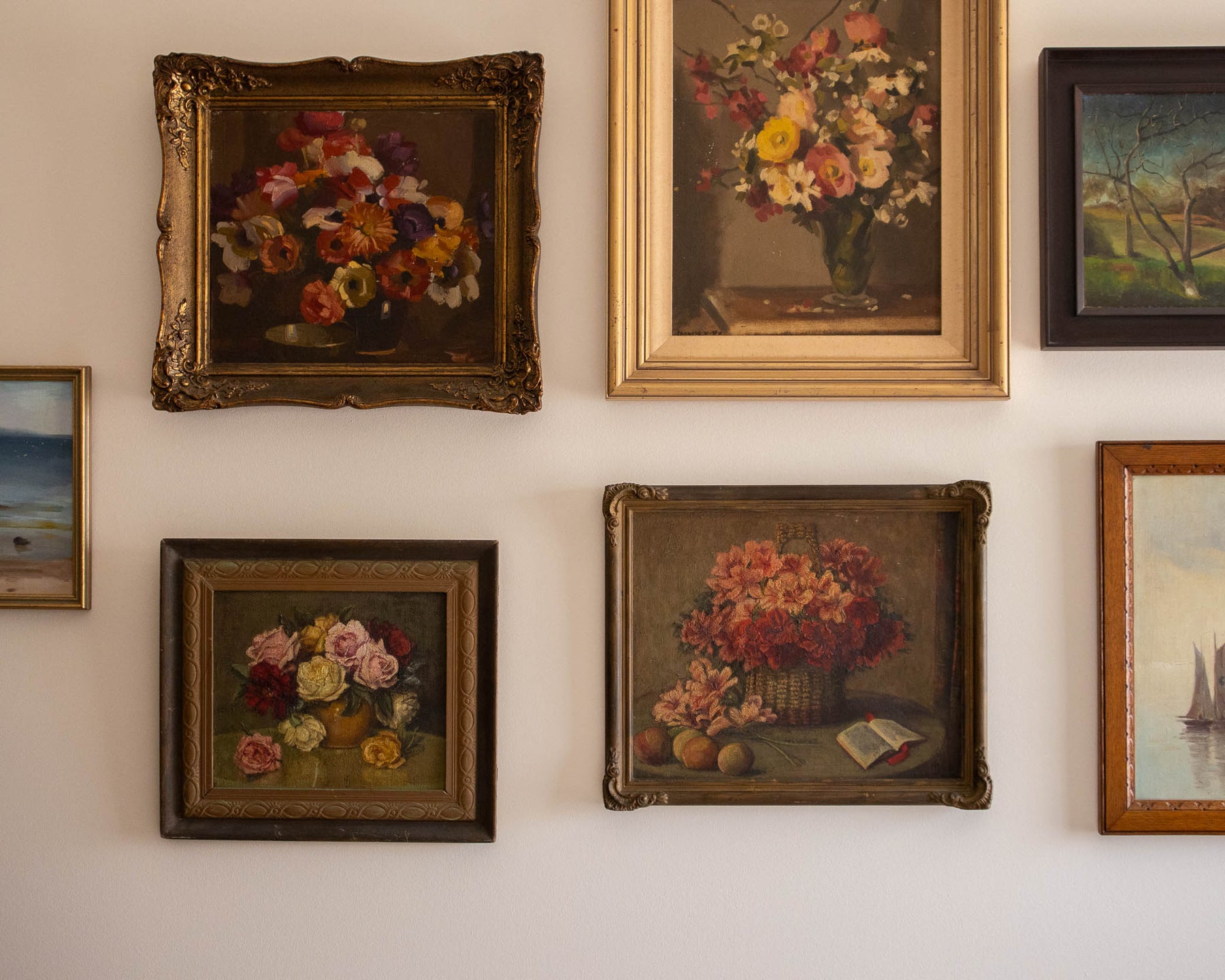 Collection of framed paintings on a wall featuring floral still lifes.