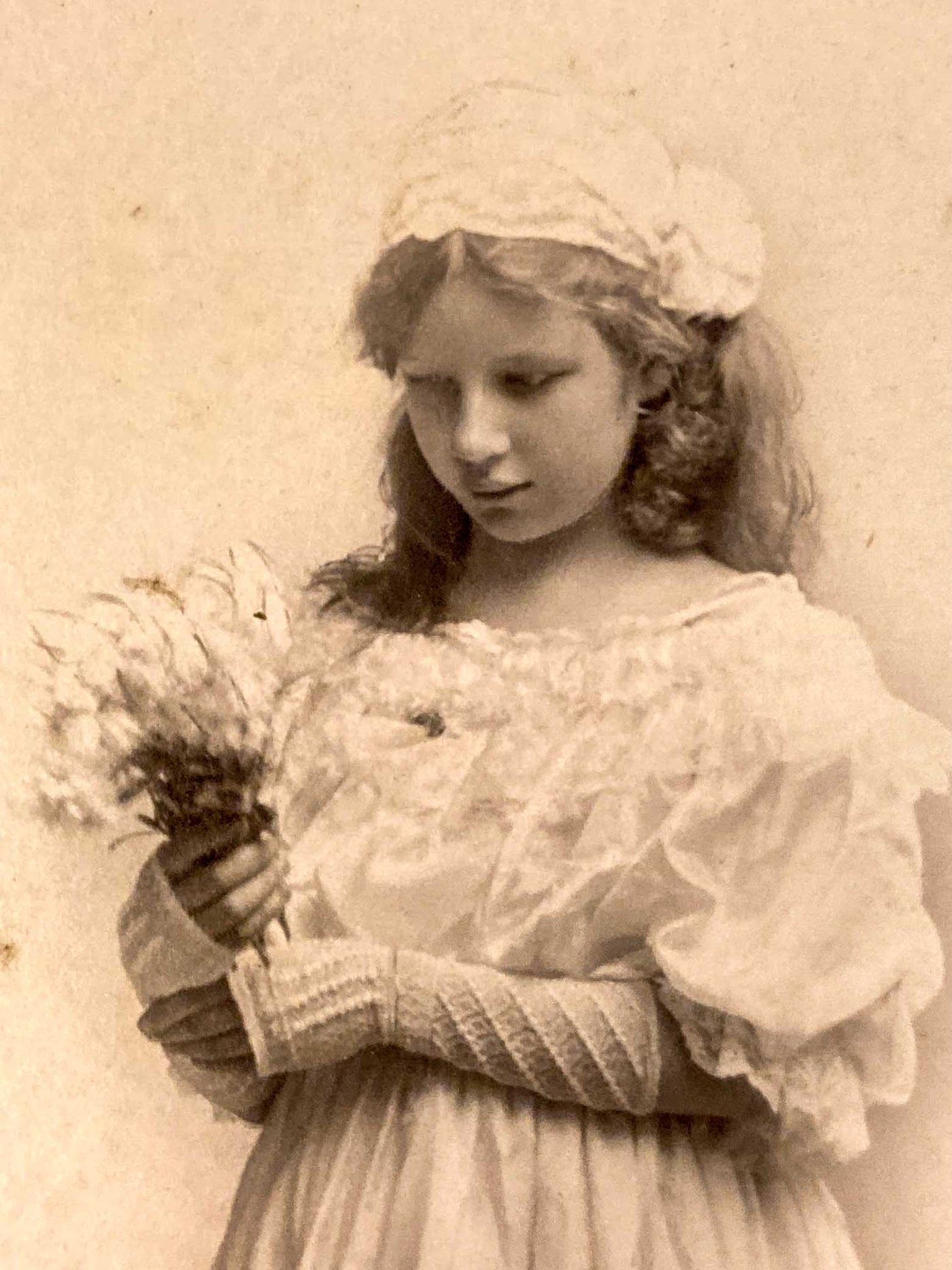 Vintage photograph of a young girl in a white dress and hat holding a bouquet.