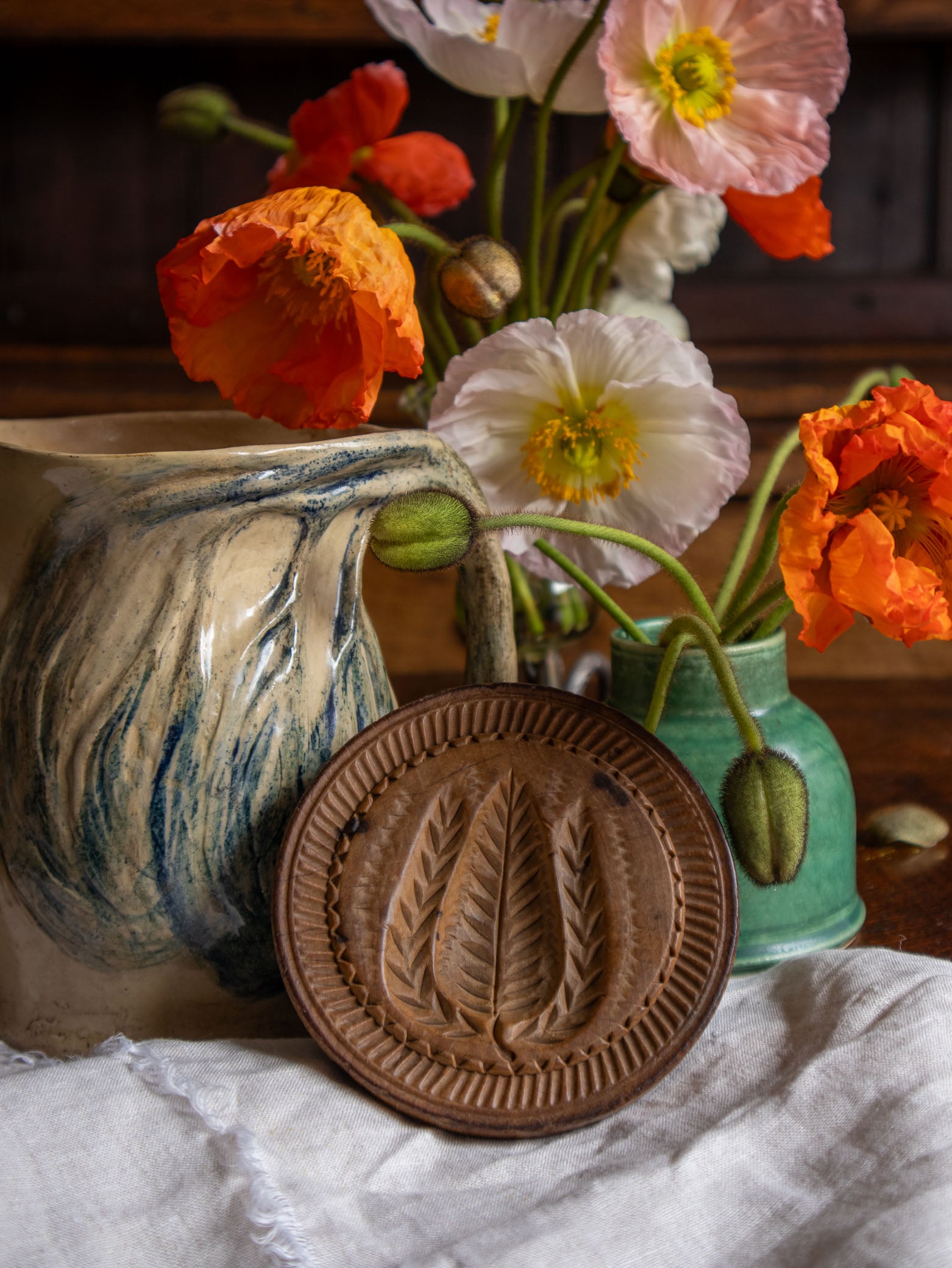Ceramic jug with floral arrangement and antique butter stamp on a wooden surface
