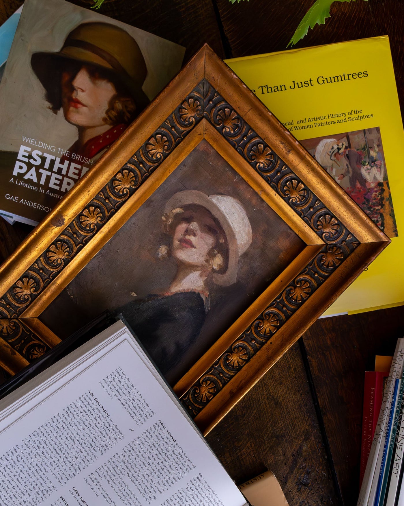 Decorative gold-framed portrait of a woman with a hat on a table with books and papers.
