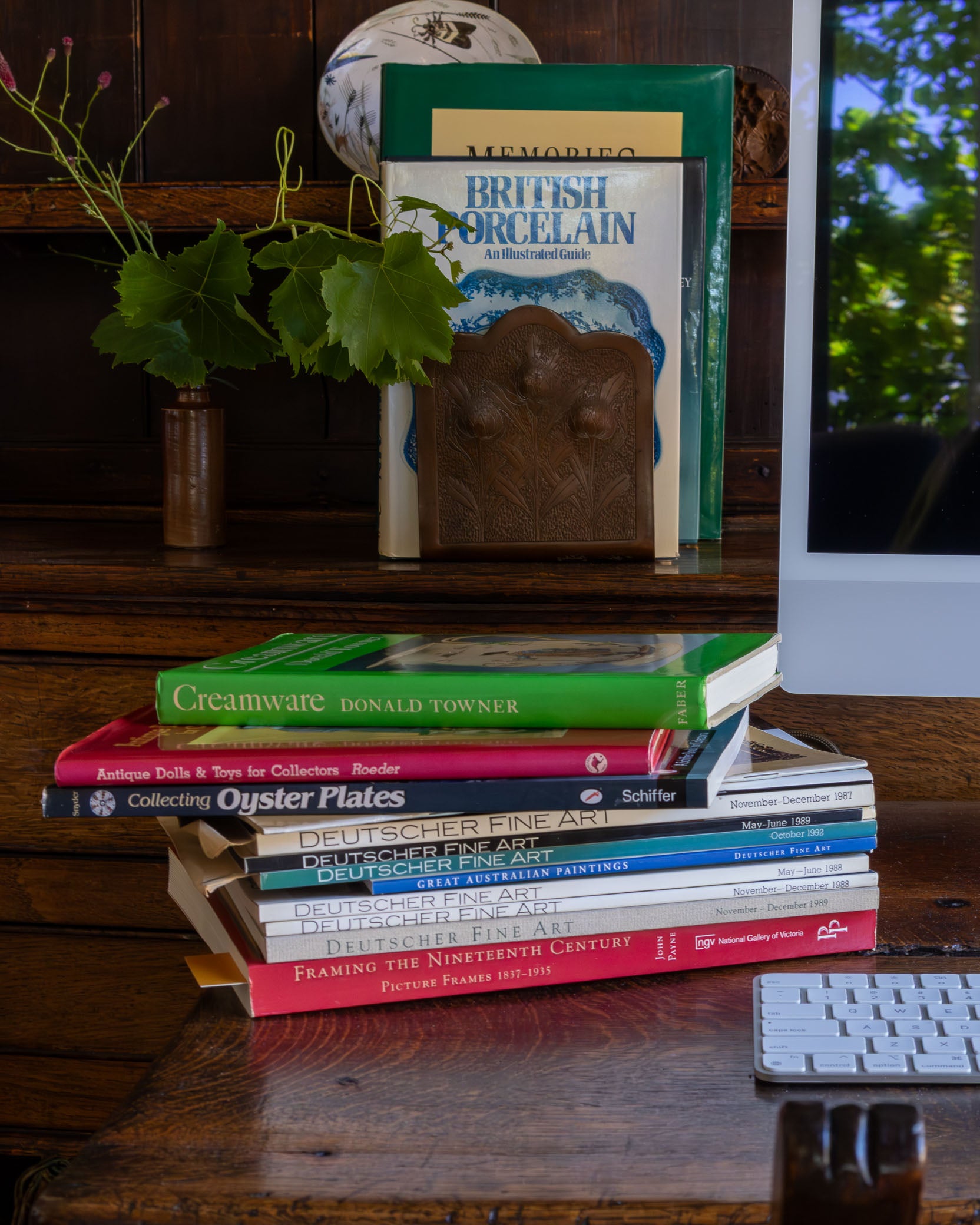 Stack of books on a wooden surface with a plant and keyboard in the background